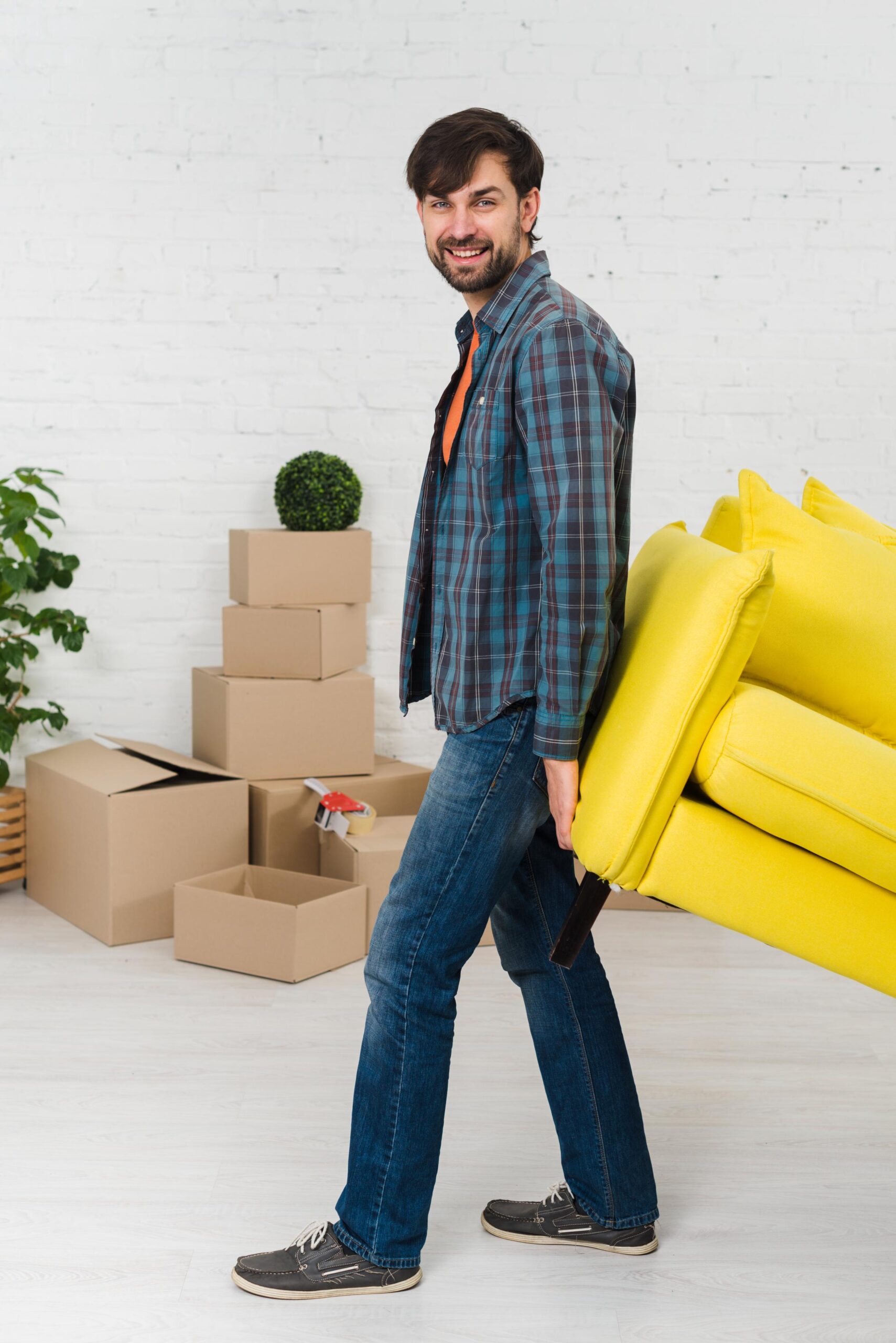 smiling portrait young man lifting yellow sofa new house
